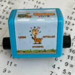 DotasToys Optellen Stempel met Dotas de Giraf op blauwe stempelhouder, getoond op rekenblad met sommen
